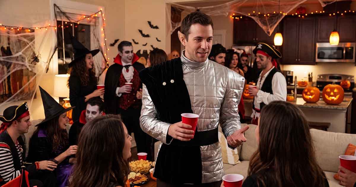 Man wearing a silver Romulan-inspired ambassador costume with pointed ears while talking with guests at a Halloween party.