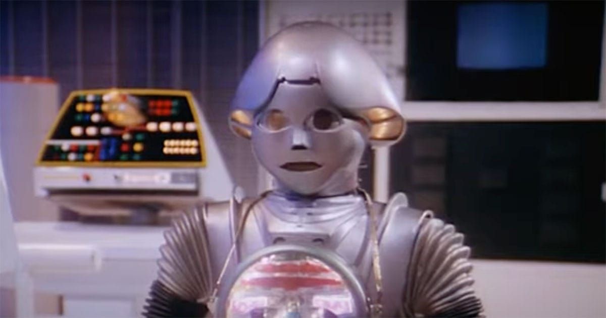 Twiki the robot from "Buck Rogers" with Dr. Theopolis on his chest in a futuristic control room.