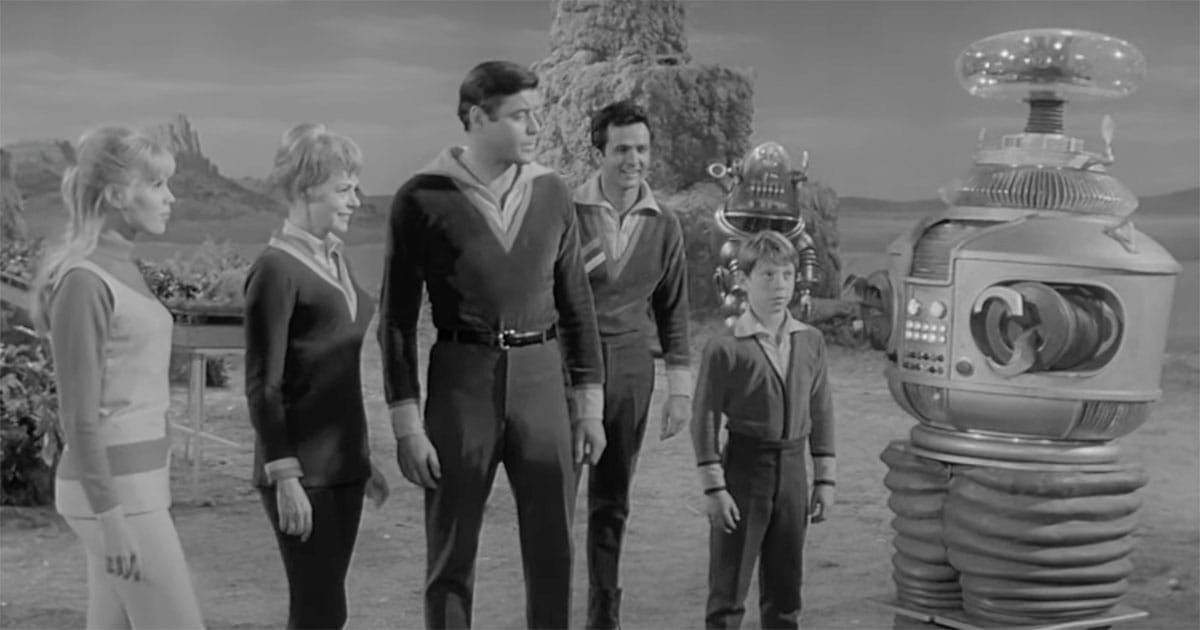 The Robinson family standing with their loyal Robot on an alien landscape in a scene from "Lost in Space."