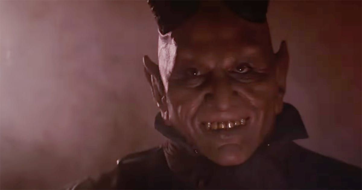 Close-up of the red-skinned, horned alien from the Mos Eisley Cantina scene in "Star Wars" (1977), smiling eerily in low light.