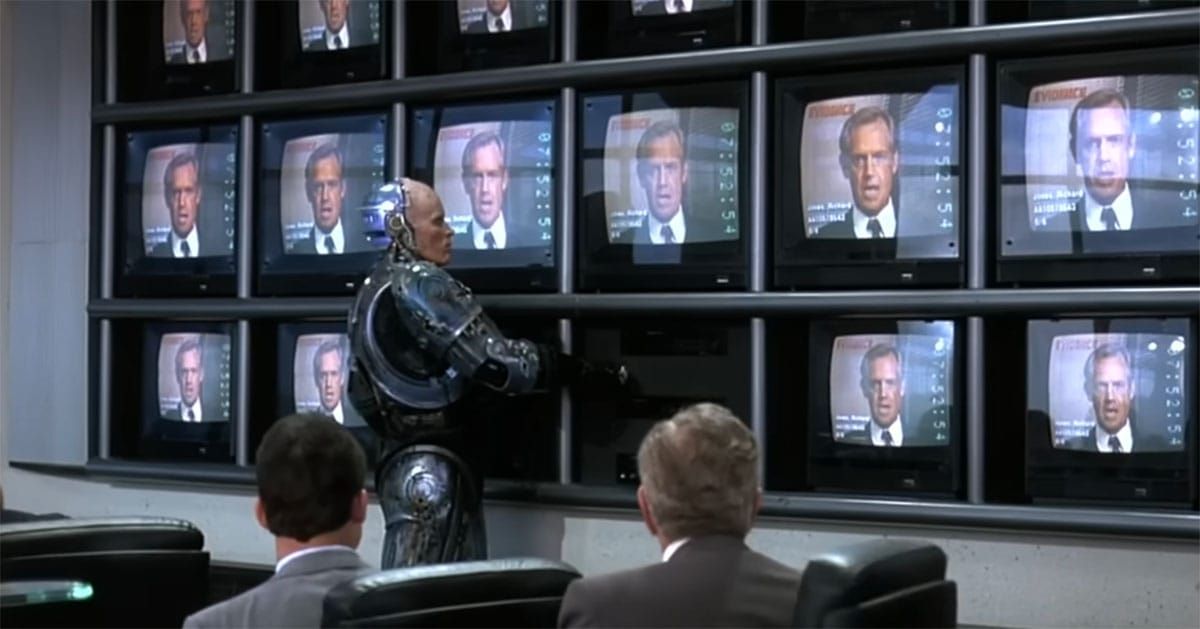 RoboCop stands before a wall of television screens showing an OCP executive, symbolizing corporate control over law enforcement in the 1987 science fiction film.