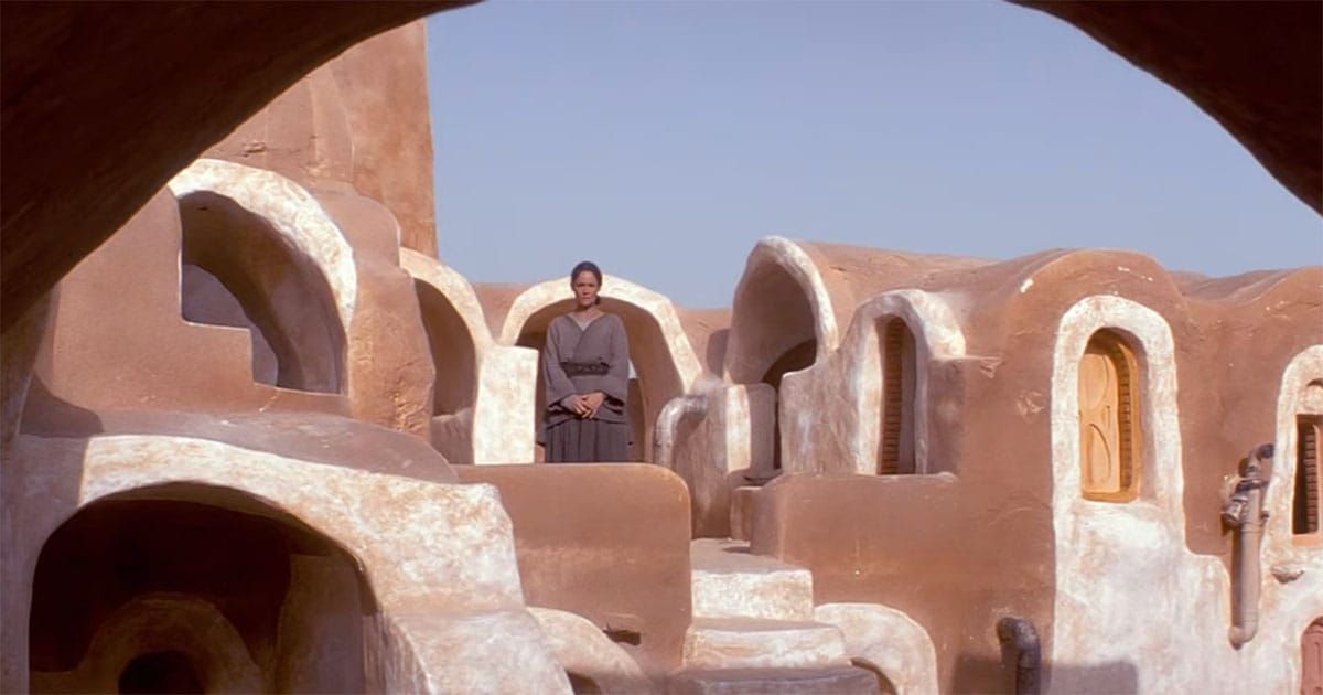 Shmi Skywalker standing alone among the clay dwellings of Tatooine.