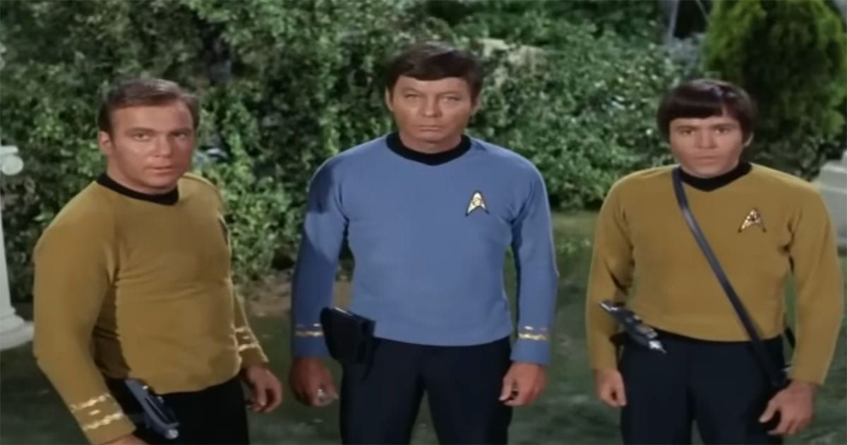 Three Star Trek original series officers standing outdoors with visible phasers and handheld equipment, wearing gold and blue uniforms during a field mission.