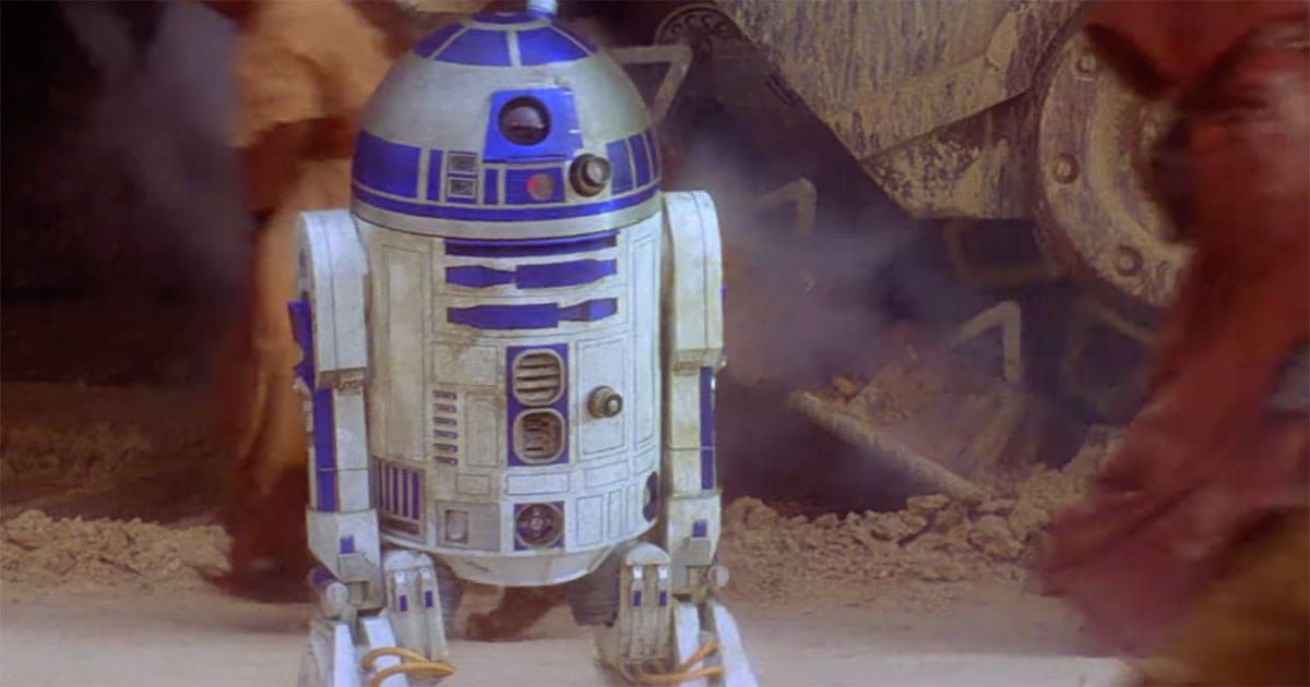 R2-D2 stands in front of a sandcrawler surrounded by Jawas in a desert scene from "Star Wars"