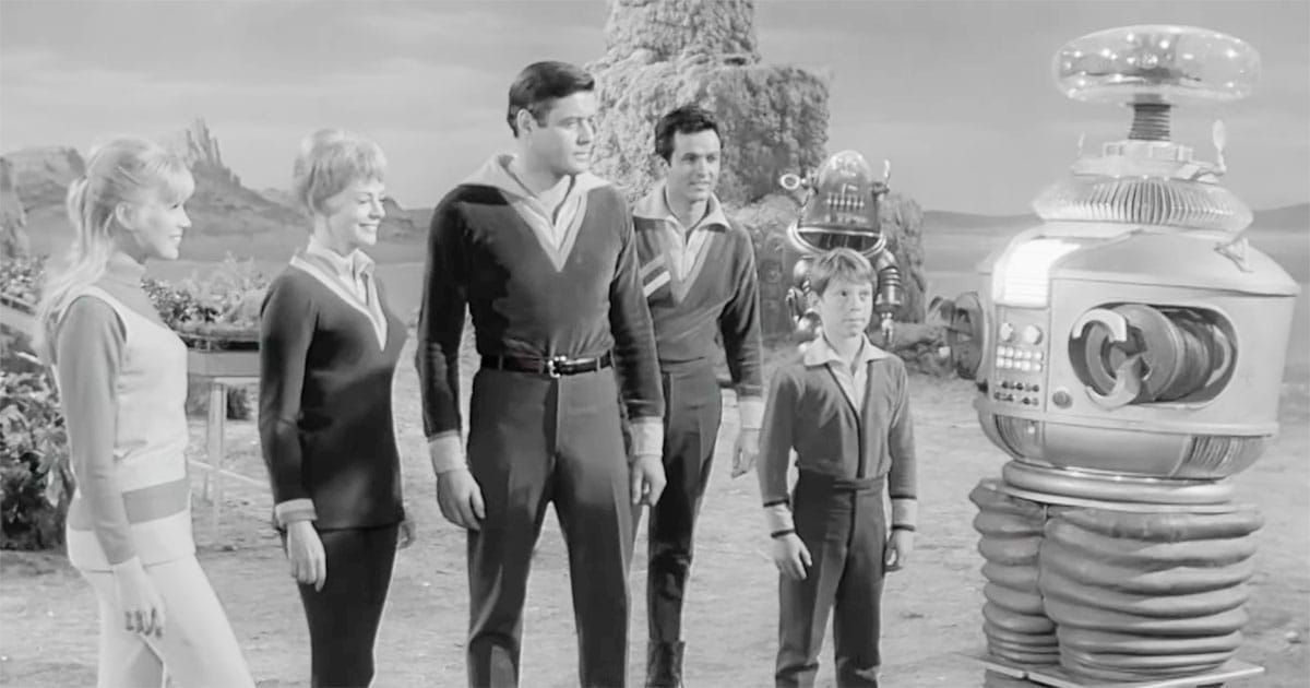Black-and-white scene from "Lost in Space" showing the Robinson family standing with their Robot companion B-9 on an alien landscape.
