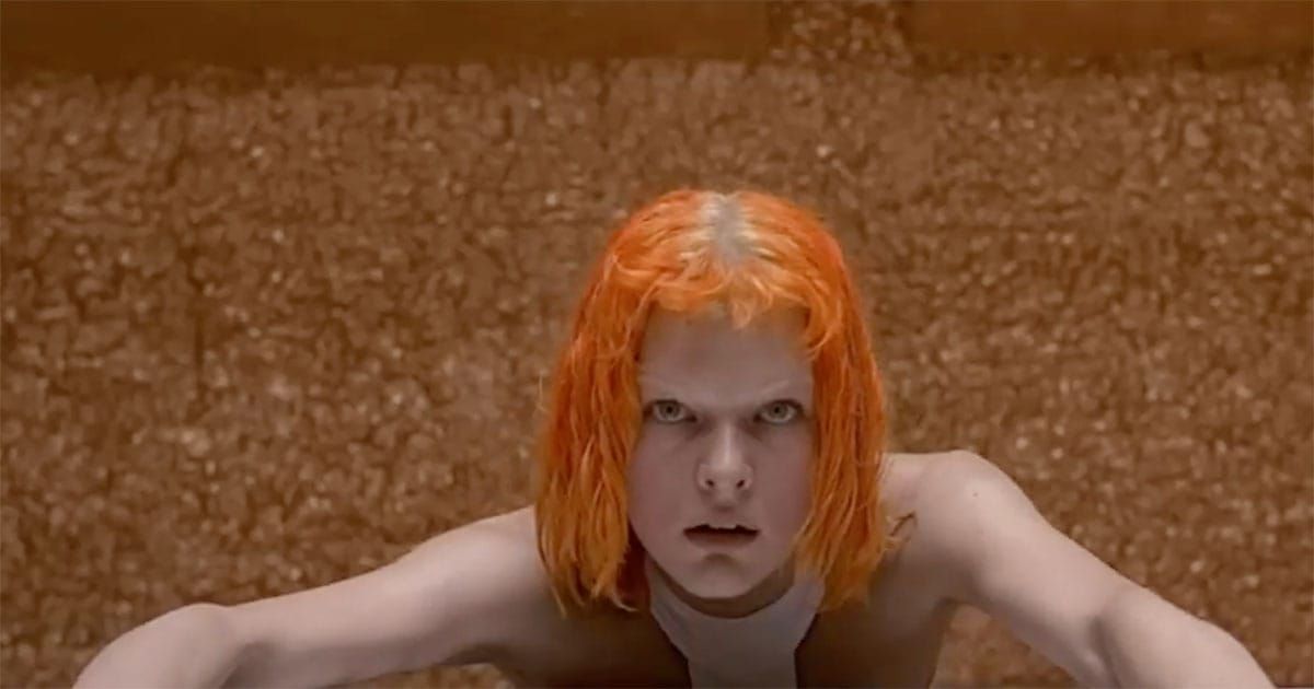 Leeloo with bright orange hair staring forward after emerging in futuristic chamber in The Fifth Element.