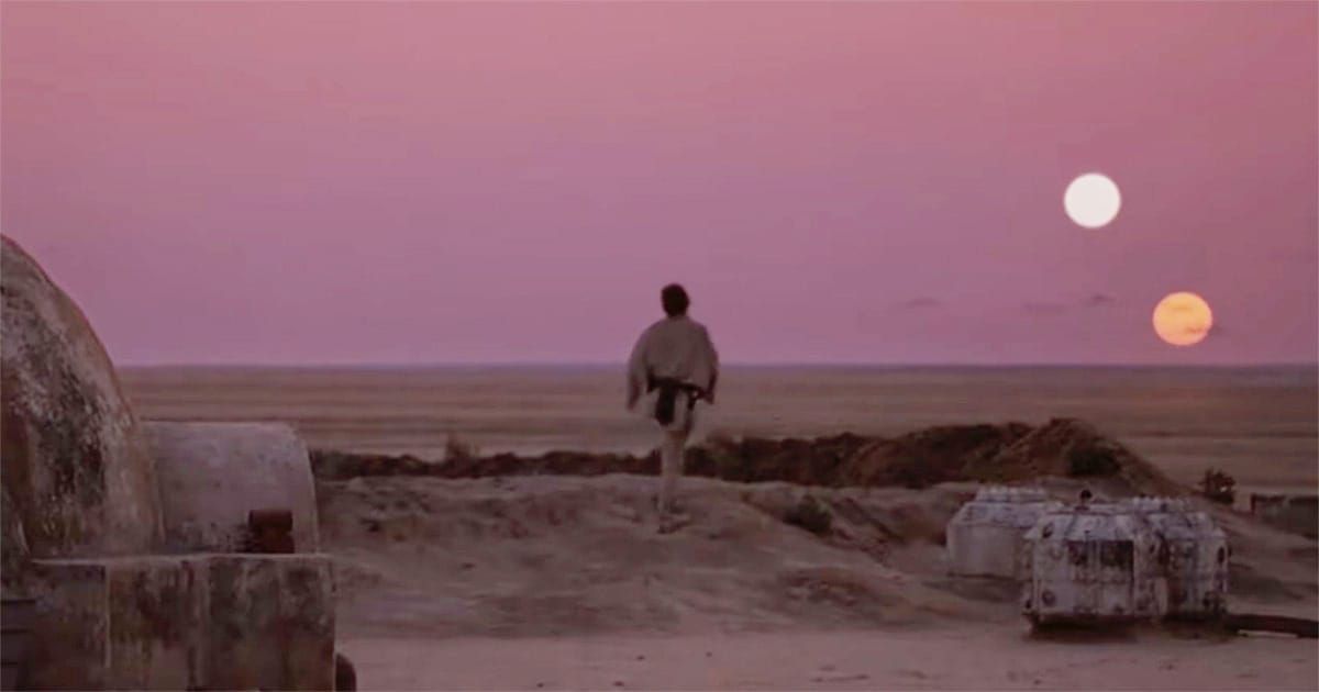 A lone young man stands outside a desert homestead and watches twin suns sink below the horizon.
