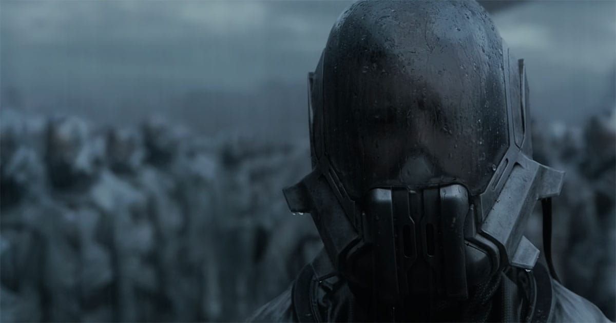 Close view of a helmeted Sardaukar soldier standing before rows of blurred imperial troops under a dark sky.