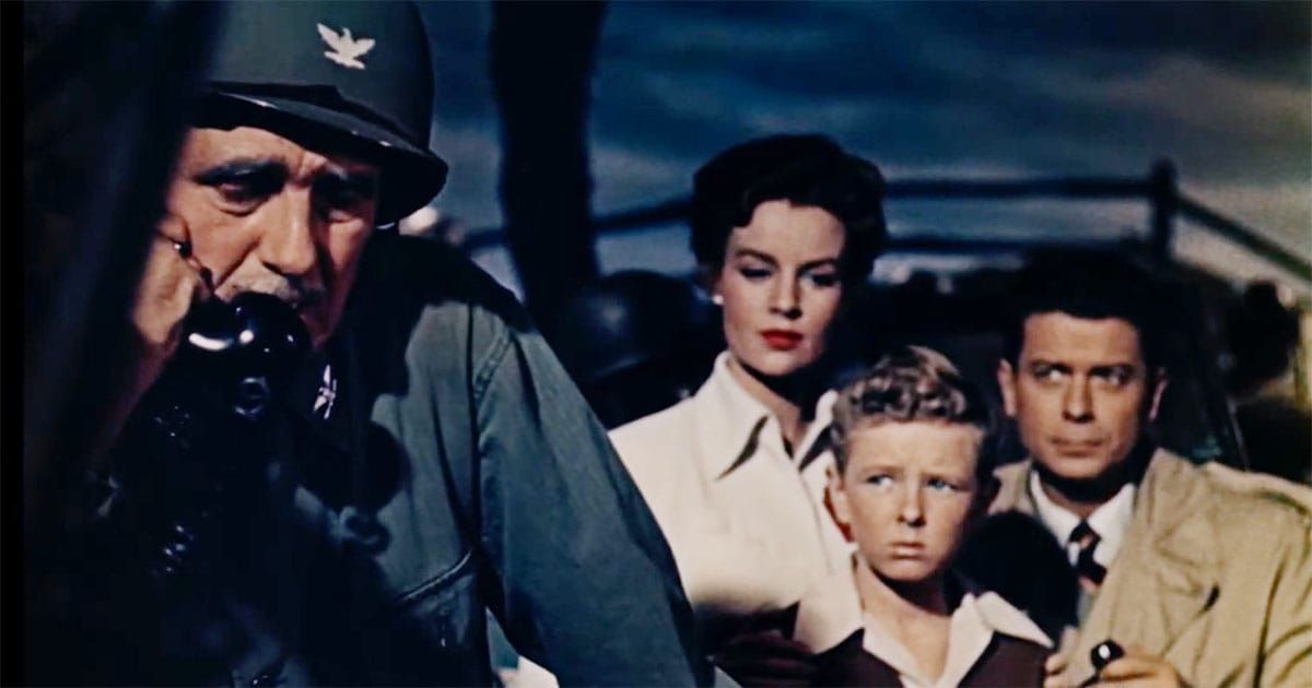 Scene from "Invaders from Mars" showing a military officer speaking on a telephone while a concerned family, including a young boy, stands behind him.