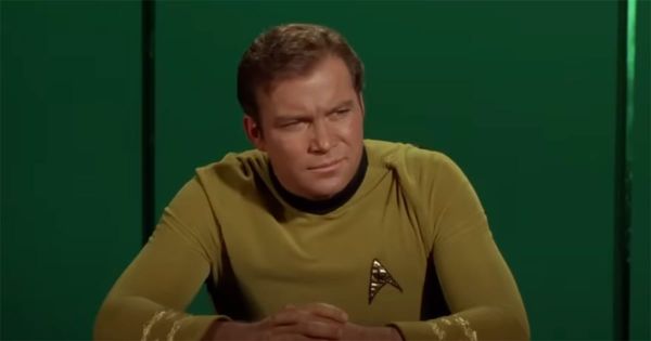 Captain Kirk seated in gold uniform against green background from "Star Trek"
