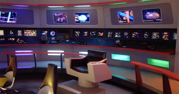 Wide view of the original "Star Trek" Enterprise bridge with captain’s chair and consoles featuring colorful jelly bean buttons and futuristic displays.