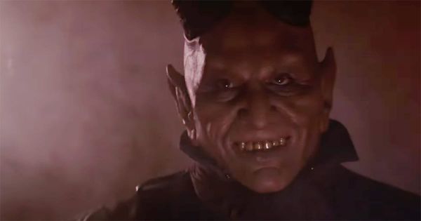 Close-up of the red-skinned, horned alien from the Mos Eisley Cantina scene in "Star Wars" (1977), smiling eerily in low light.