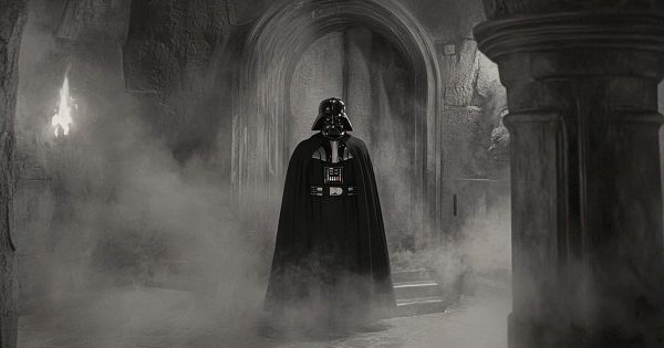Darth Vader standing alone in black armor and cape inside a stone corridor filled with smoke.