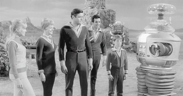 Black-and-white scene from "Lost in Space" showing the Robinson family standing with their Robot companion B-9 on an alien landscape.
