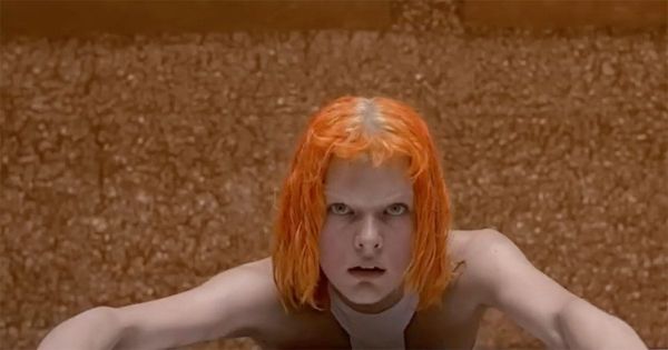 Leeloo with bright orange hair staring forward after emerging in futuristic chamber in The Fifth Element.