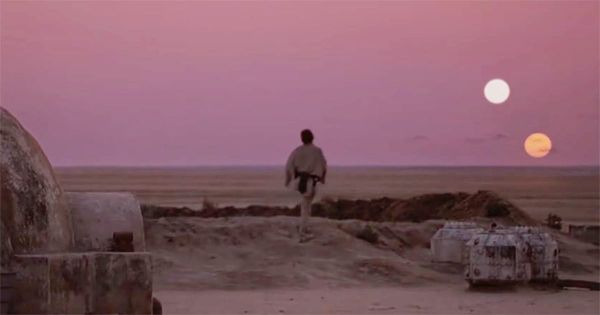 A lone young man stands outside a desert homestead and watches twin suns sink below the horizon.