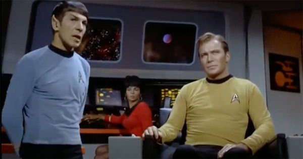 Captain Kirk and Mr. Spock on the bridge of the Enterprise with Uhura at her station and space visible beyond them.