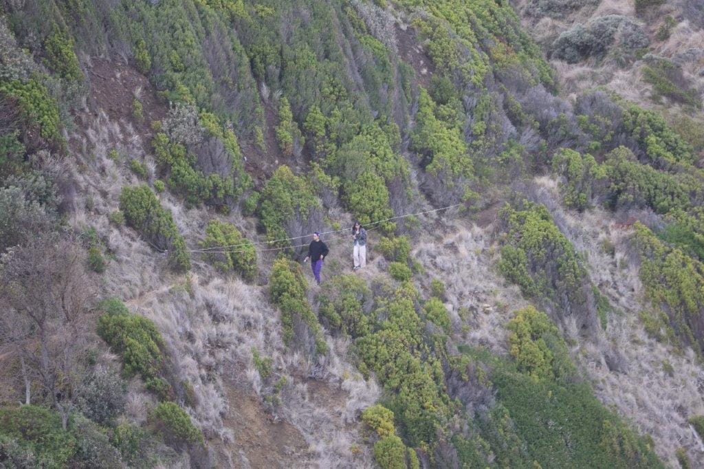 Visitors to Punch Bowl Rocks scale the narrow track leading down the cliff to the rocks with a small dog leading  the way.