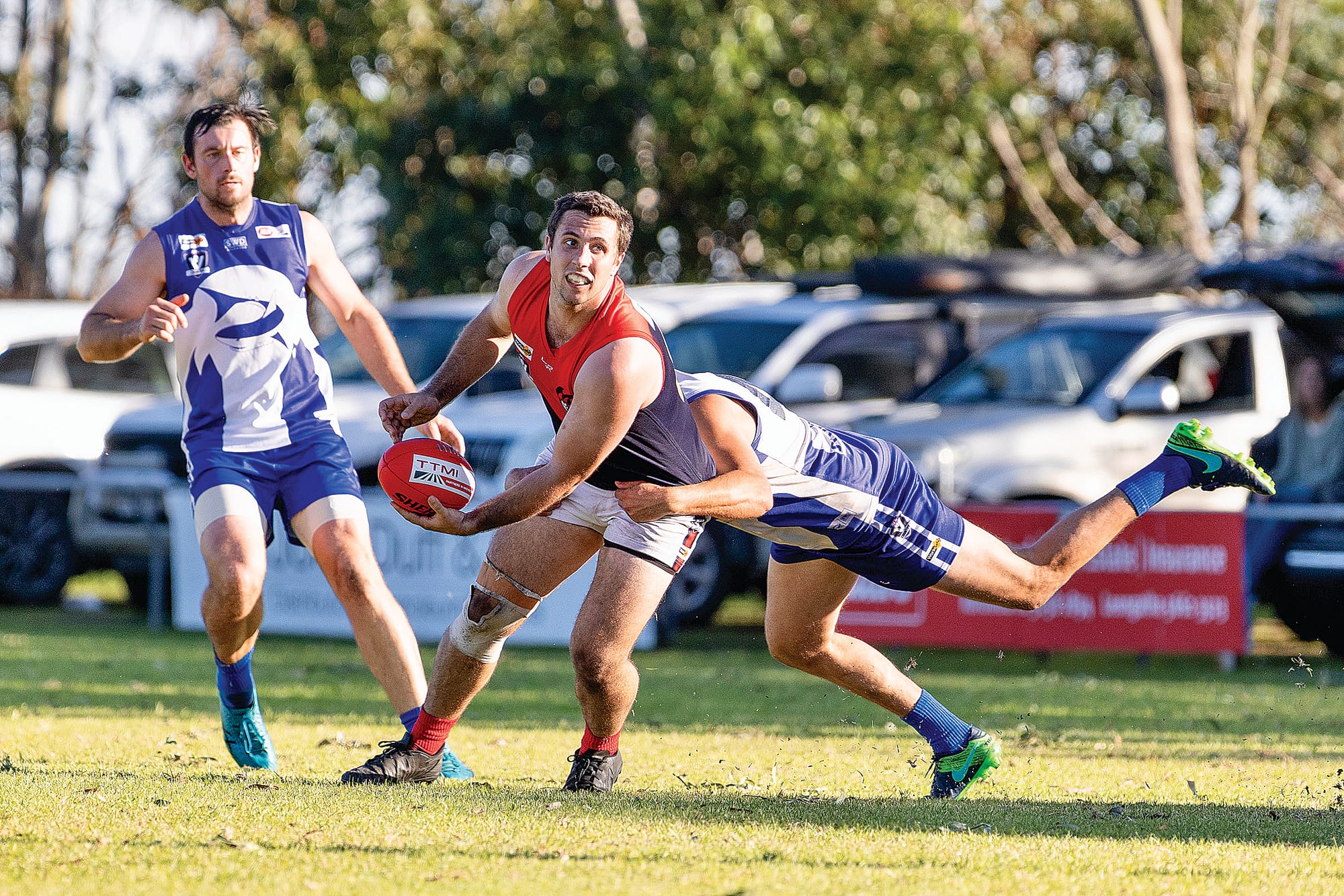 Ben Perry looks to handball the Sherrin as his Sharks opponent tackles from behind.