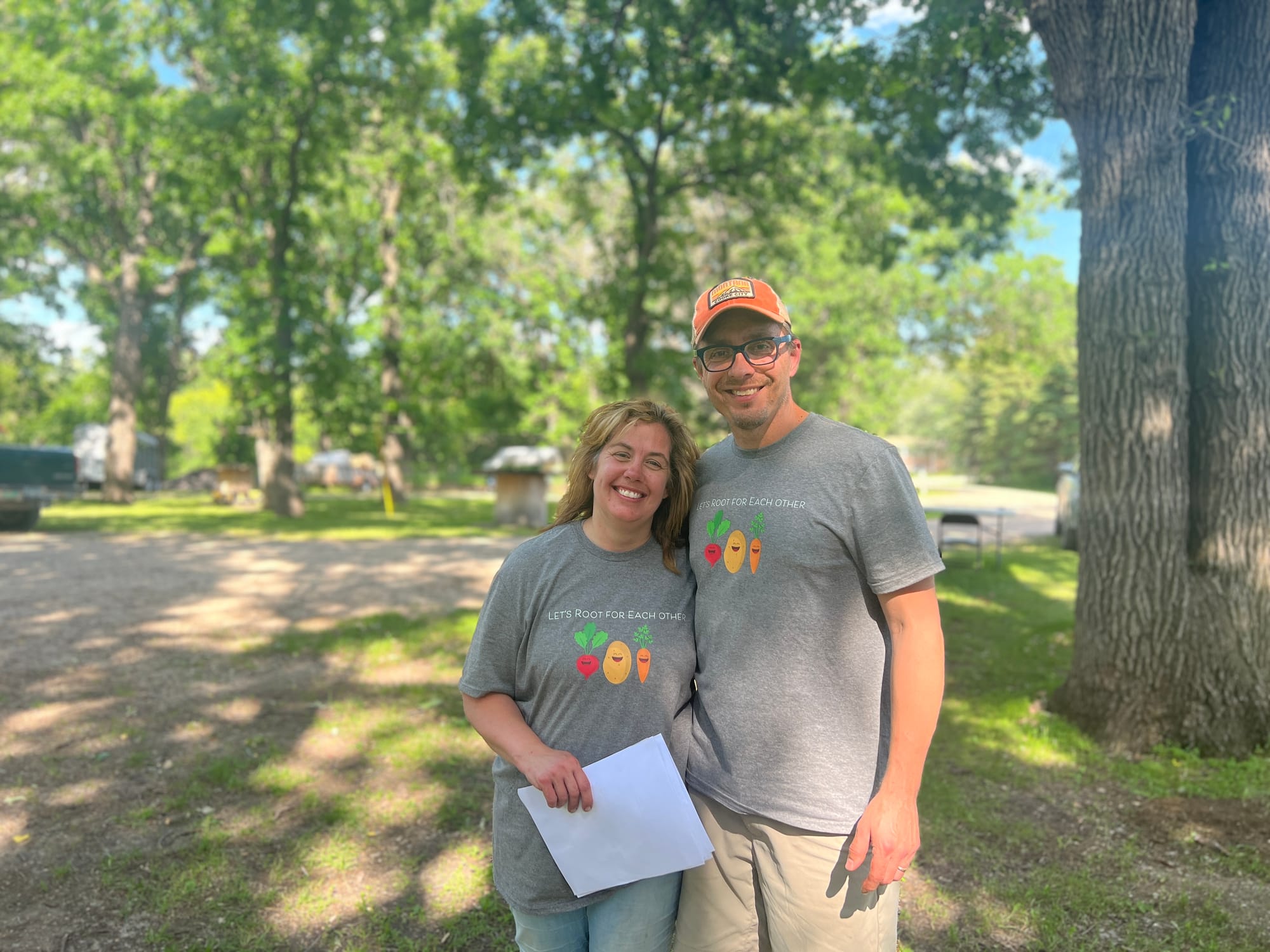 Woman and man pose for a photo under trees on their property.