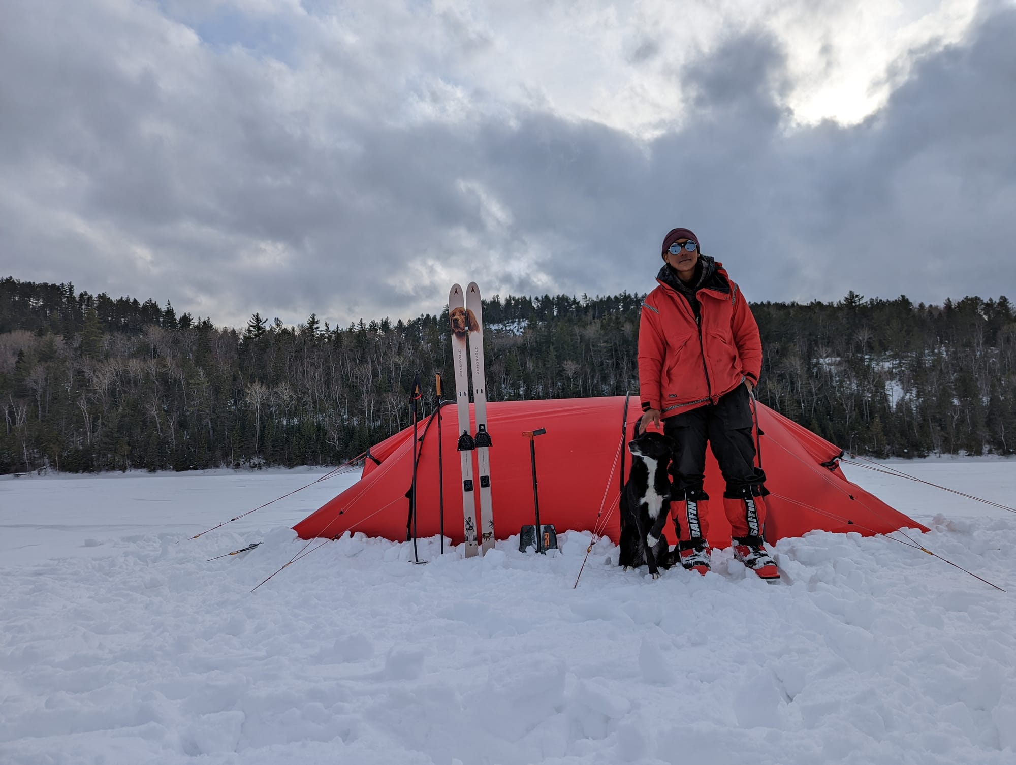 Woman poses with her dog in front of a tent in the snow.