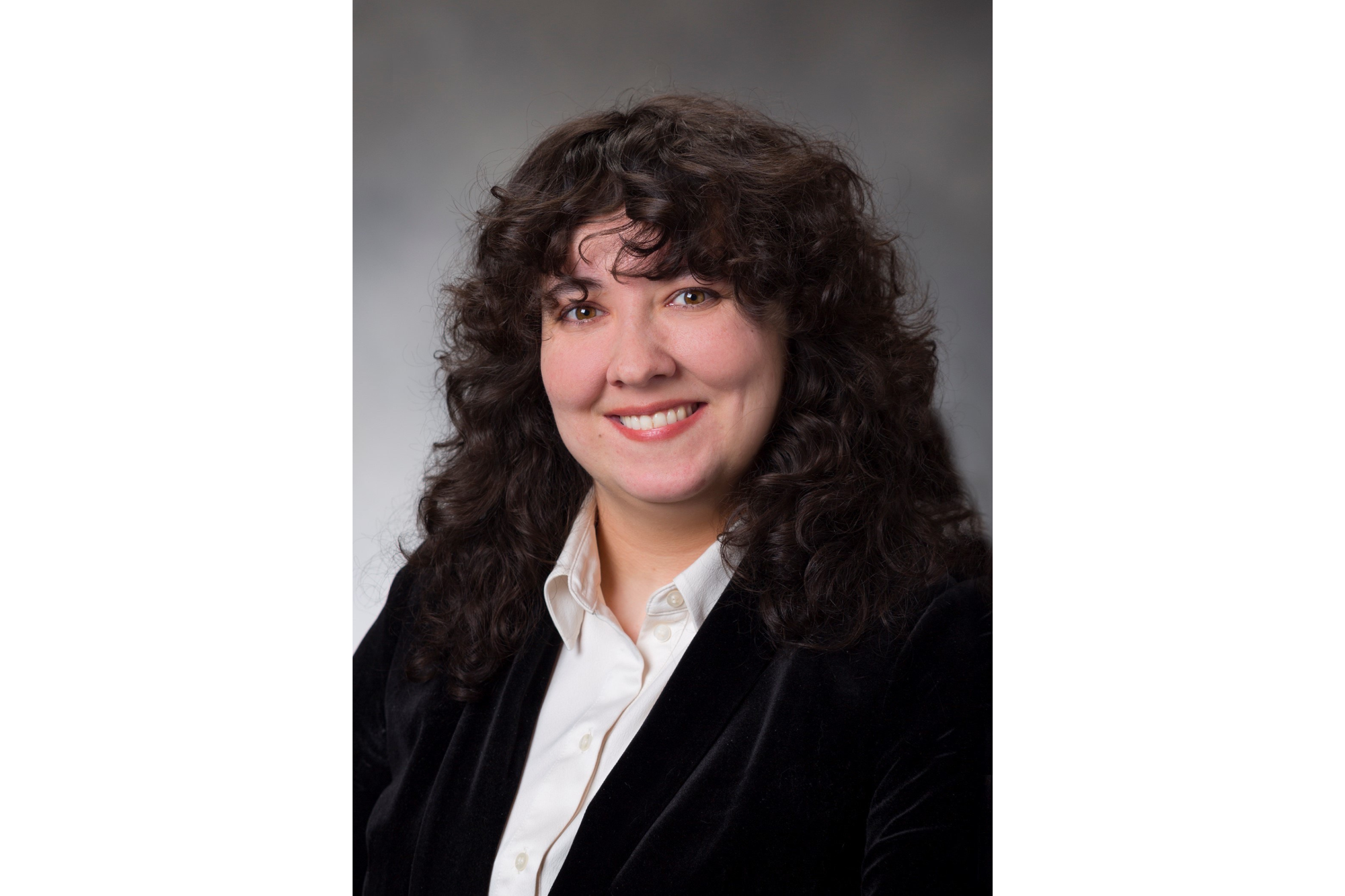 Woman with dark, curly hair poses for a professional portrait.