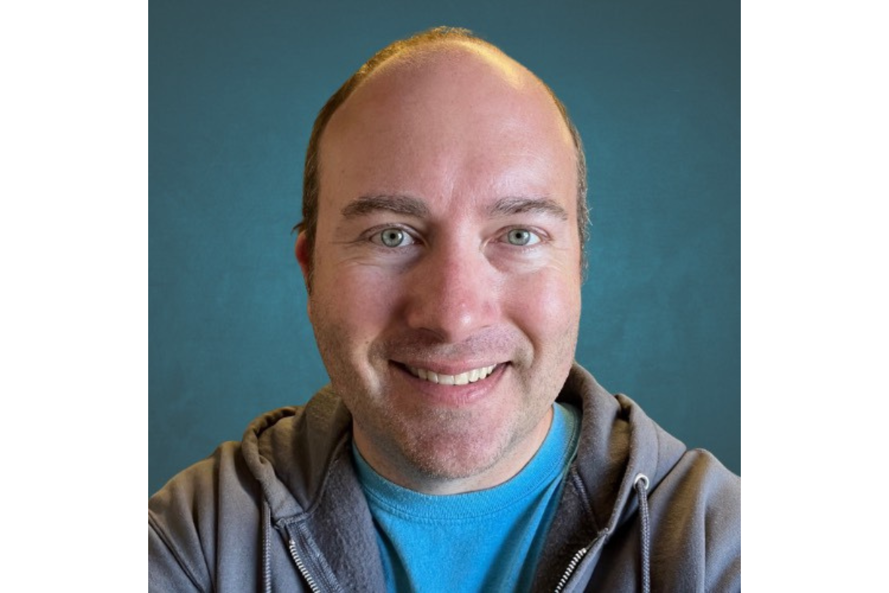Man wearing a T-shirt and hoodie smiles for a selfie.