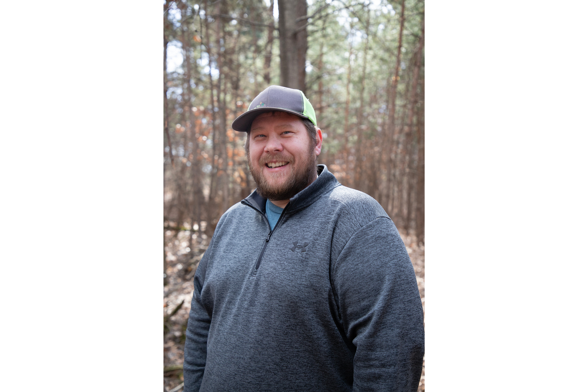 A man smiles for the camera during a biochar demonstration. He wears a grey baseball cap and black sweatshirt. 