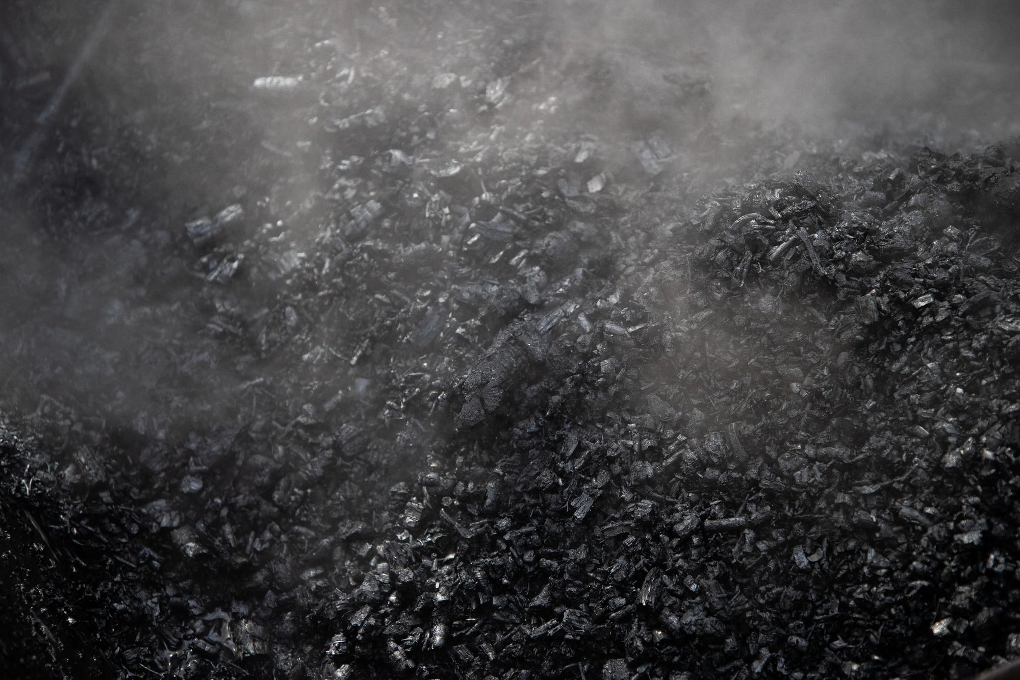 Smoke rises off black charcoal-looking material that is actually biochar. 