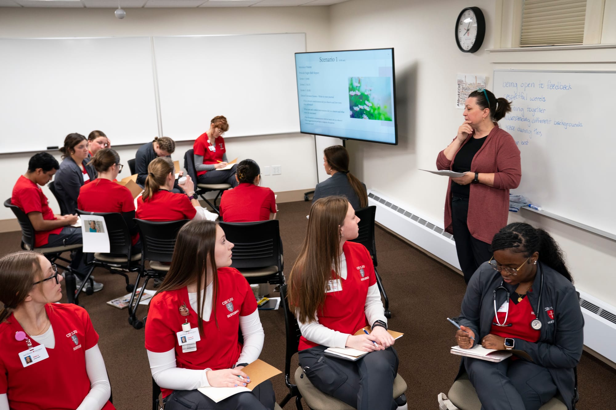 Nursing students look toward their instructor at the front of the classroom as she provides instructions on their activity. 