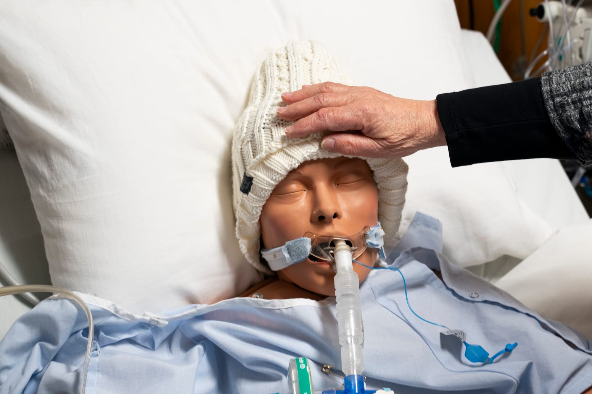 A training mannequin lays in a hospital bed and receives a blessing during an end-of-life training exercise. 