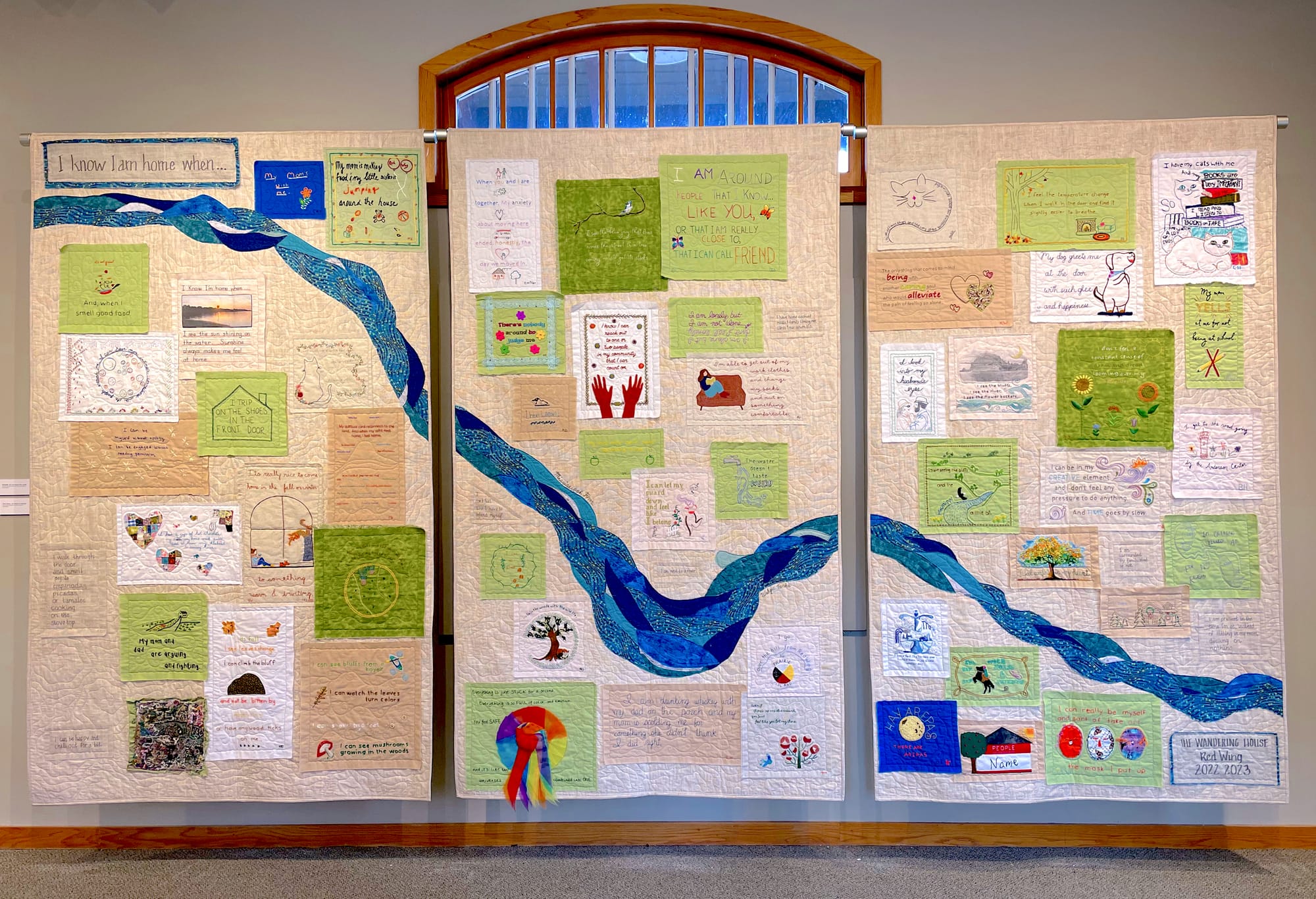 The completed embroidery project from Red Wing shows a river flowing across three panels. The embroidered squared are placed all along the river on either side. 