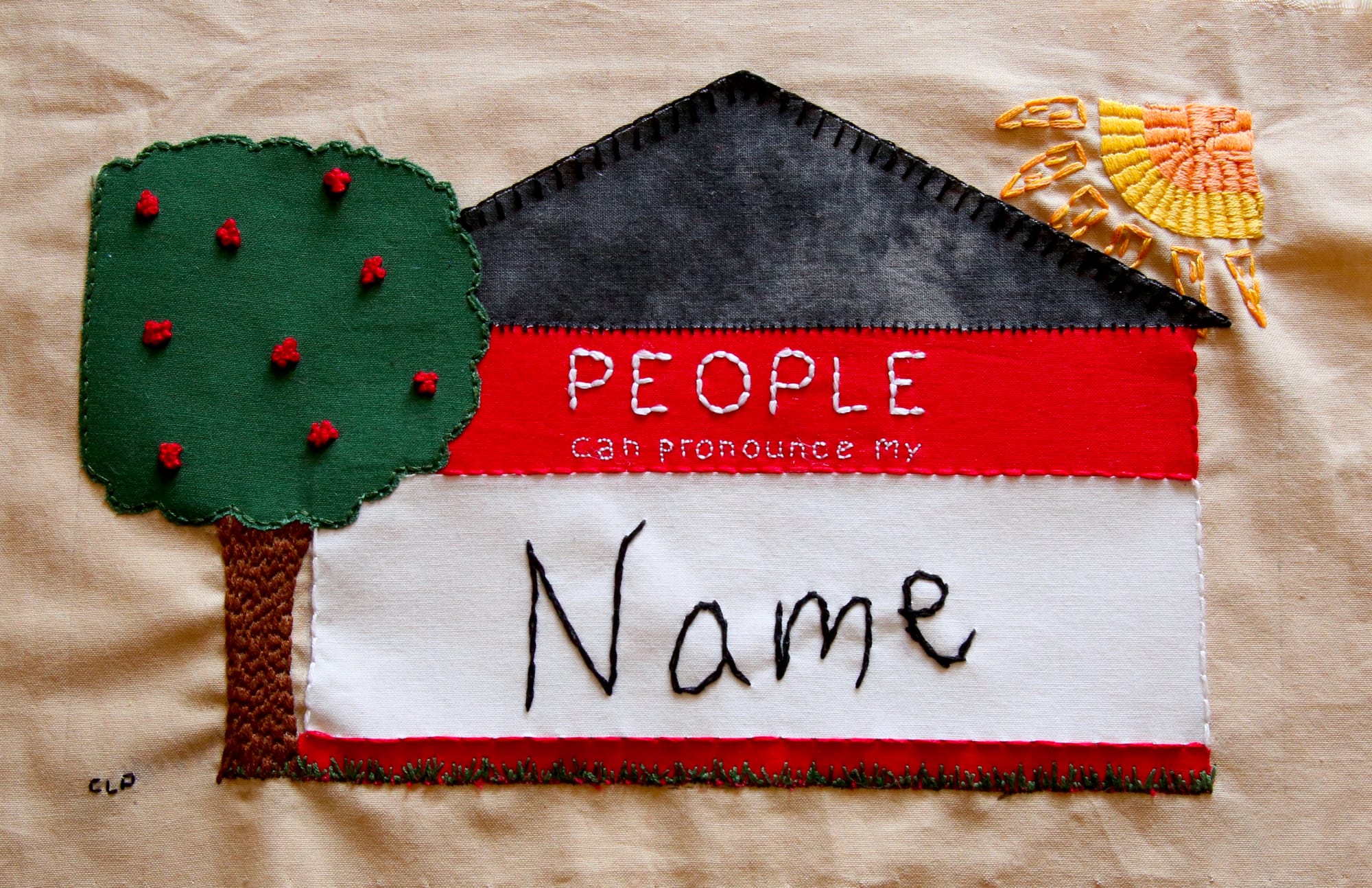 Uno de los proyectos de bordado muestra una etiqueta con forma de casa con un árbol y un sol cerca. Dice: "La gente puede pronunciar mi nombre."