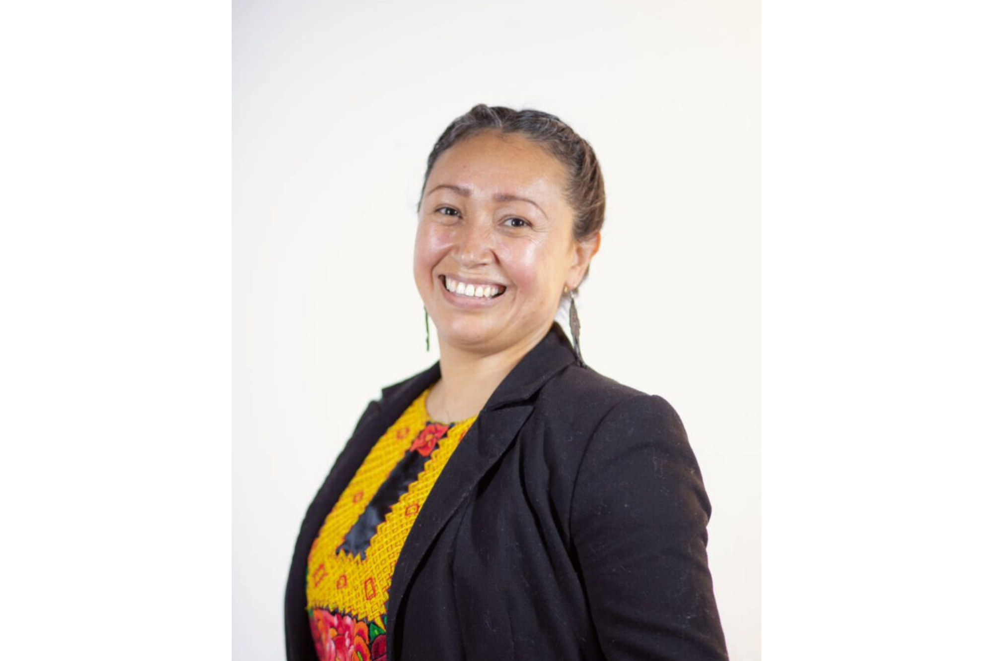 Una foto de una mujer. Ella lleva una camisa vistosa baja un blazer negro. Ella sonríe. 