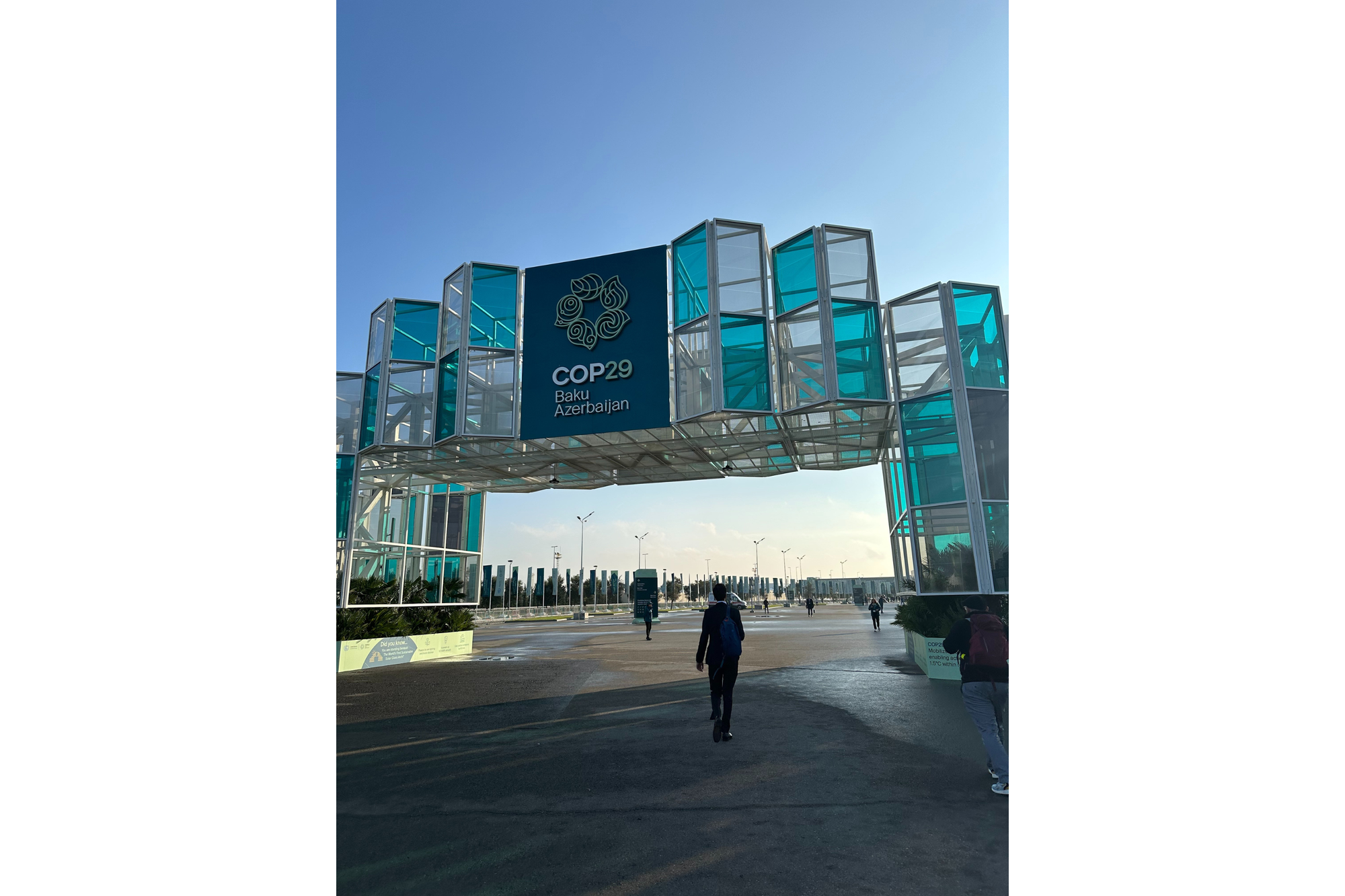A person walks toward the entrance to COP29. The entrance looks like a square arch made of clear and blue glass. 
