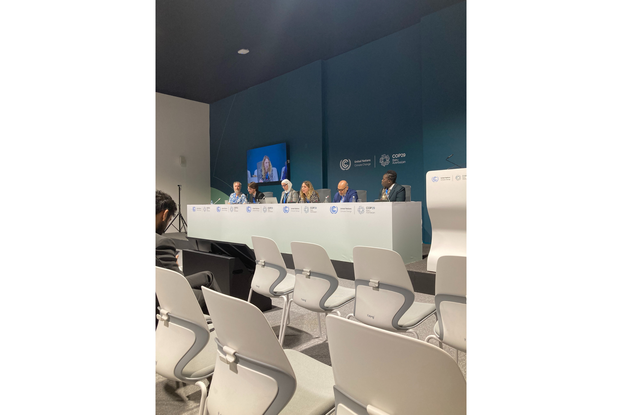 Six people sit at a table at the head of the room for a panel discussion. 