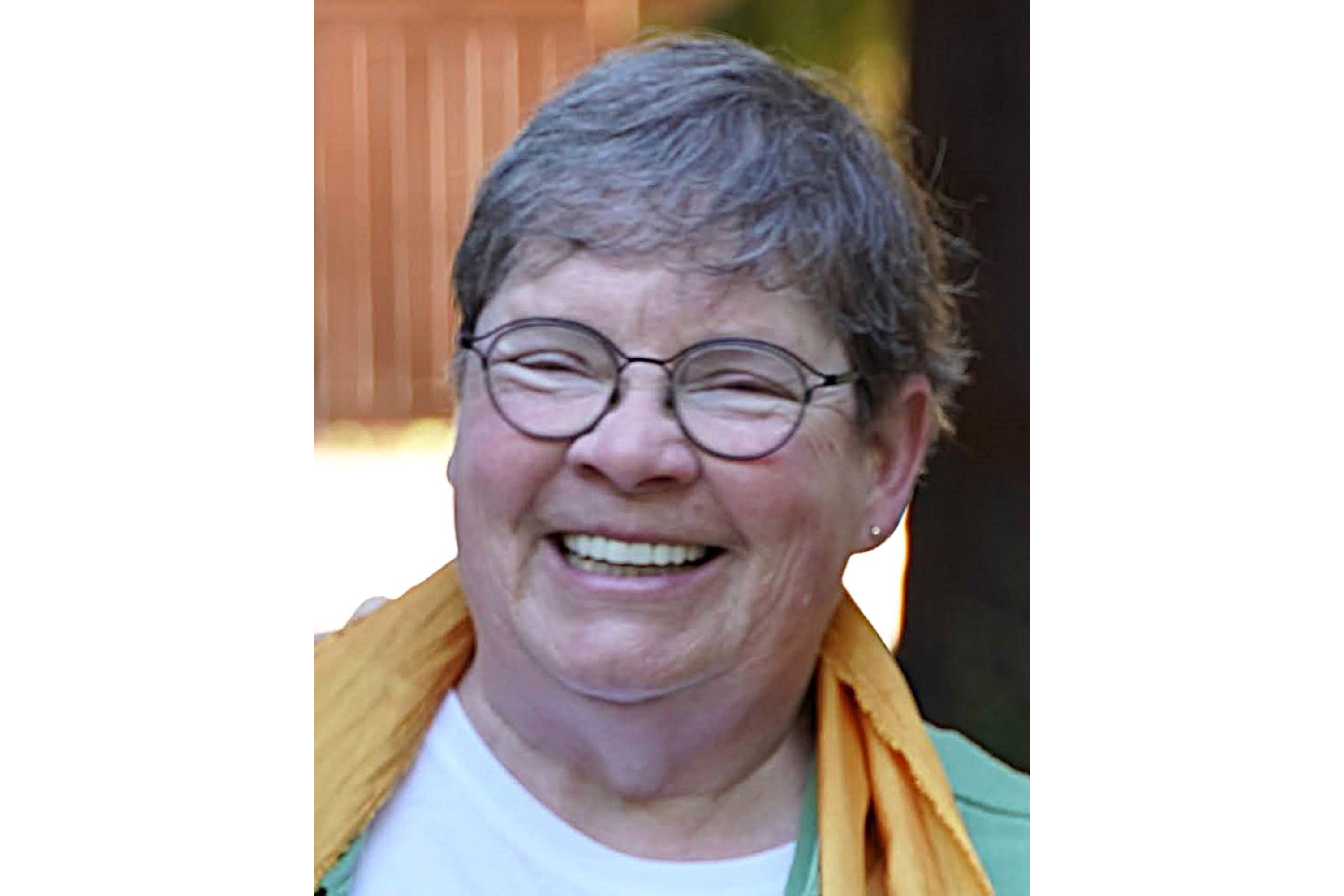 A woman smiles for a photo. She wears glasses and has short, grey hair. 