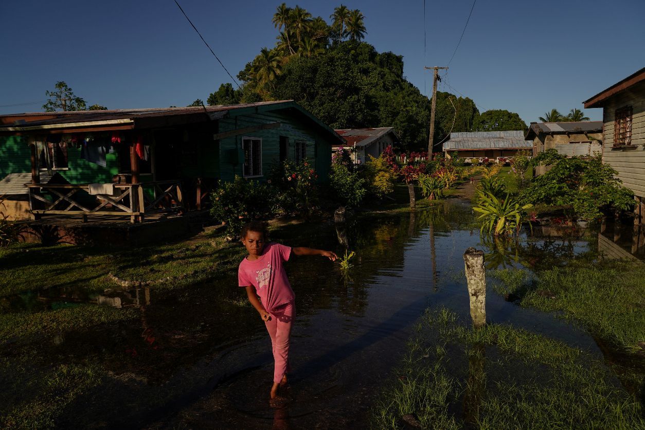 Local girl Tokasa Robanakadavu, 10, wades through seawater flooding her community during high tide in Serua Village, Fiji, July 15, 2022. As the community runs out of ways to adapt to the rising Pacific Ocean, the 80 villagers face the painful decision whether to move. (REUTERS/Loren Elliott)