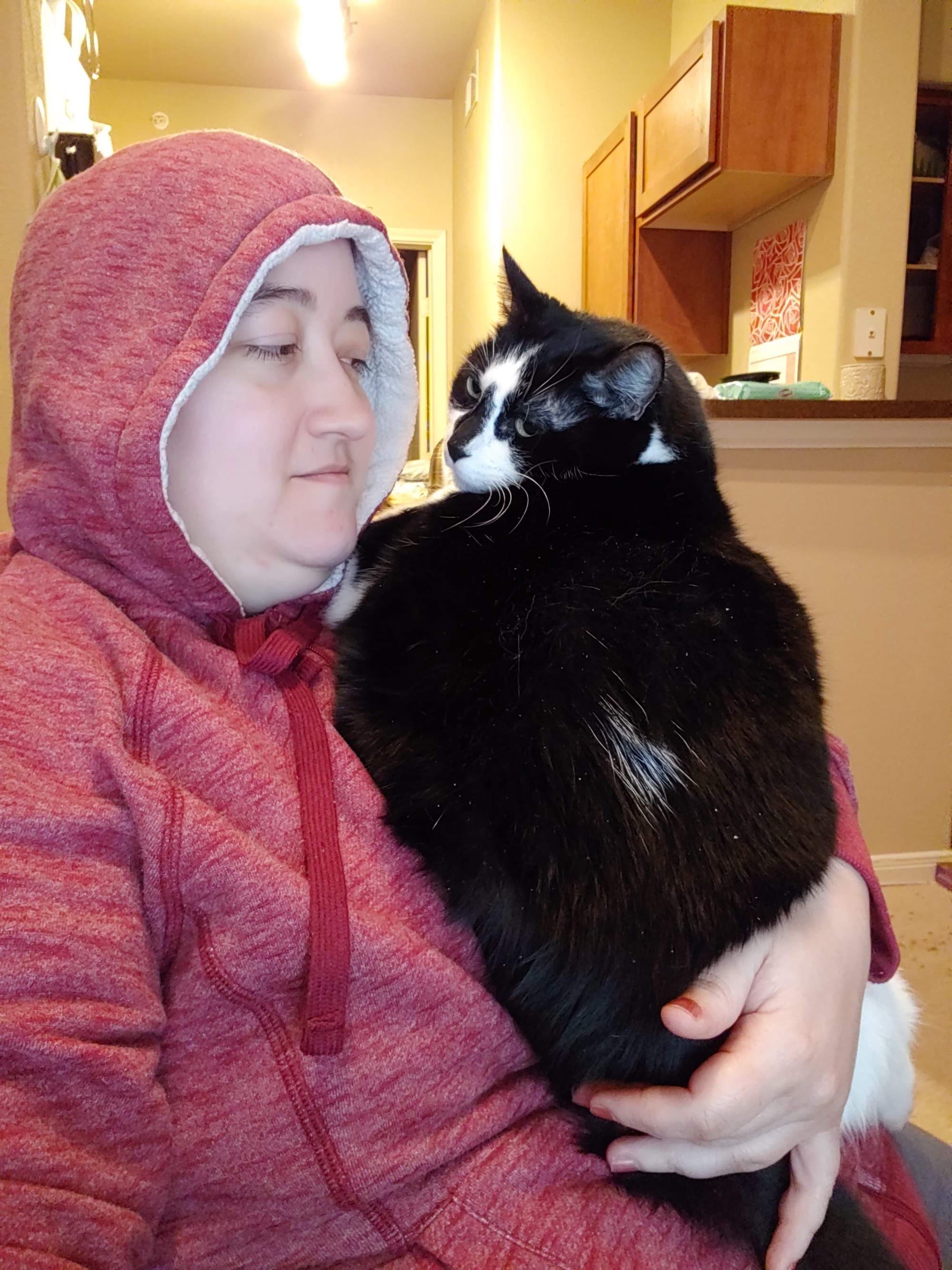Me in a red hoodie holding Rooley, a very large black and white cat with a white spot on his back.