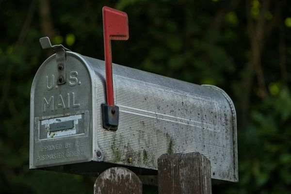 A metal US Mail residential mail box with its red flag raised
