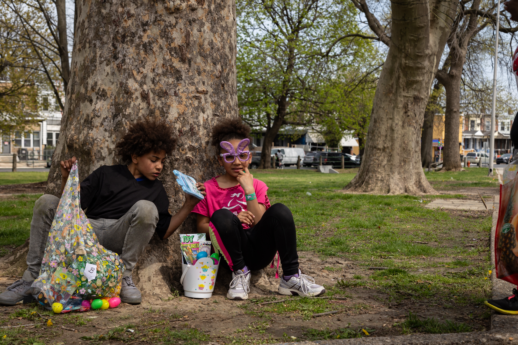 Two kids sit under a tree with Easter baskets at Harrowgate Park