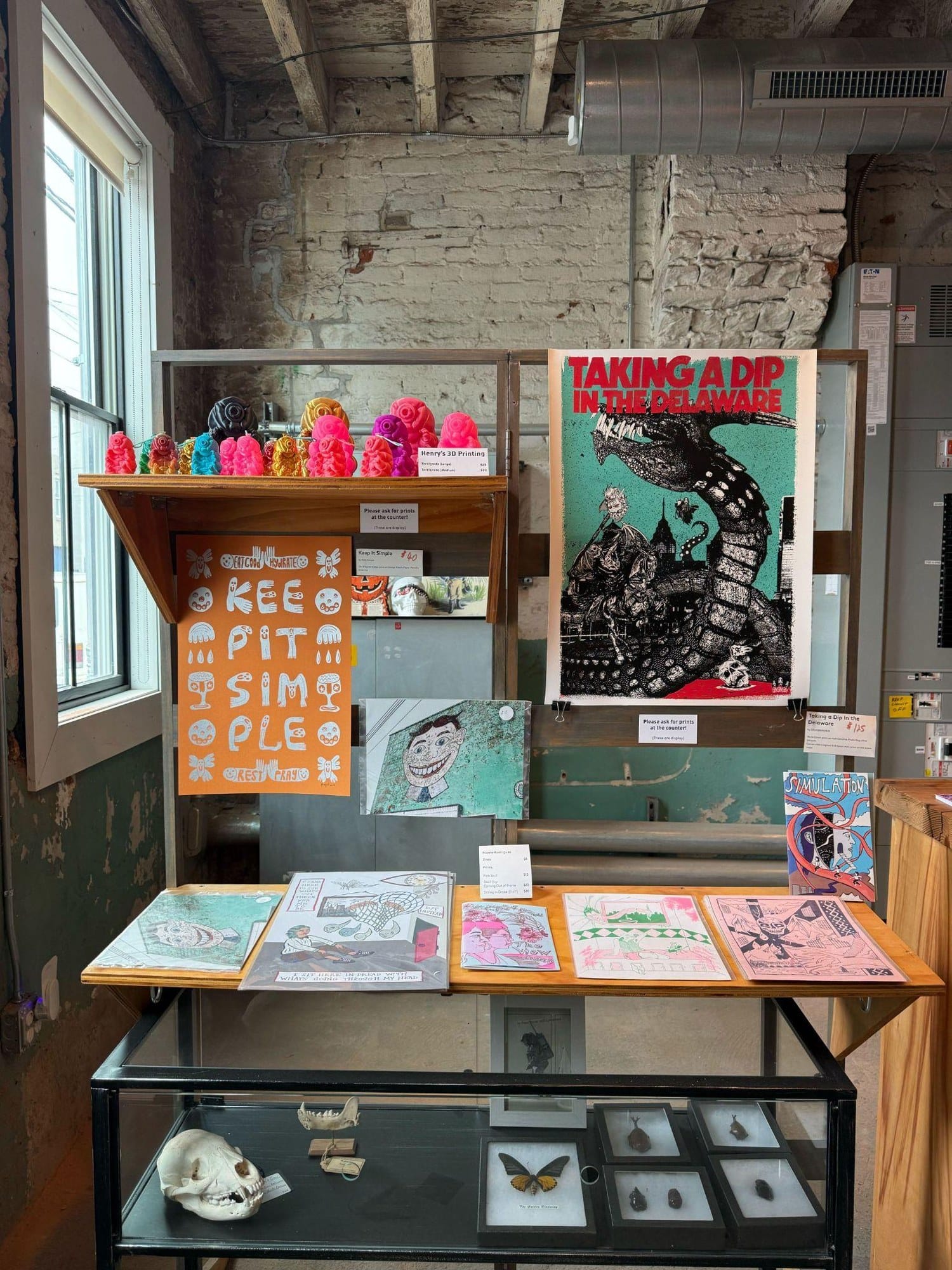 Posters, zines and small prints displayed on a wall and shelves at Fireball Printing, including a 'Taking a Dip in the Delaware' screen print.