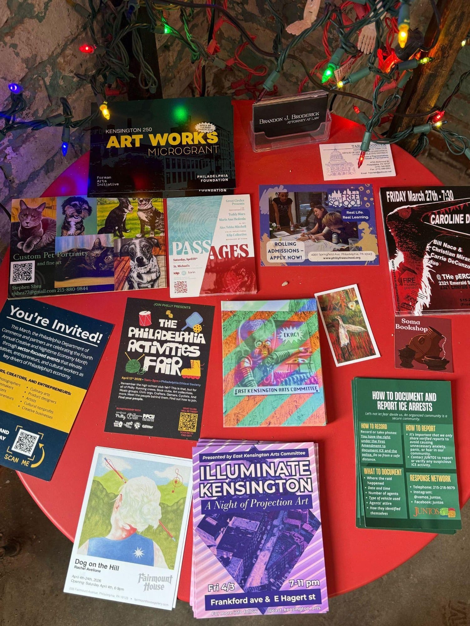 A red table at Fireball Printing covered with flyers and event cards for Kensington arts events and community resources.