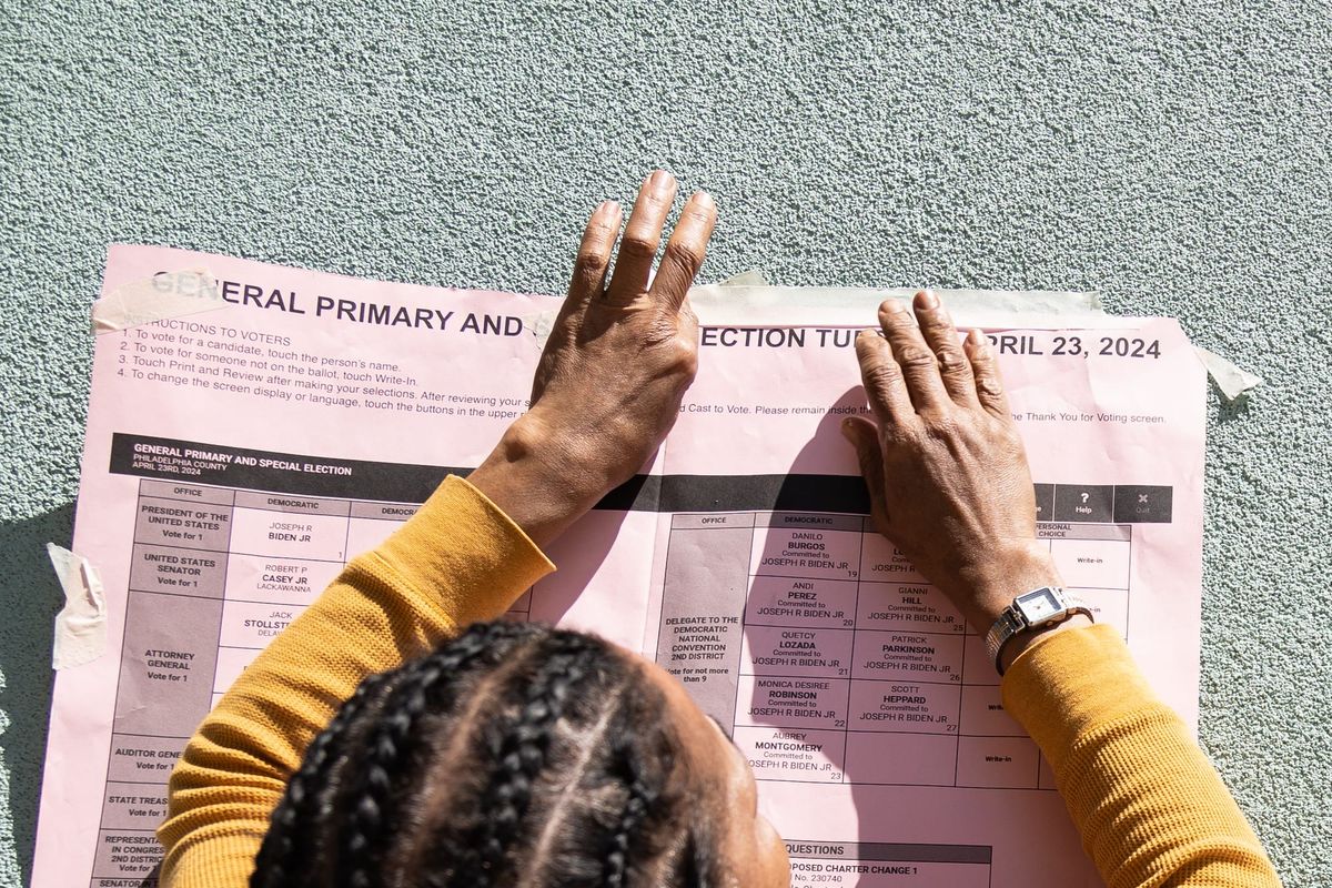 A person in a yellow sweater presses their hands against a printed sample ballot for the Philadelphia primary election.