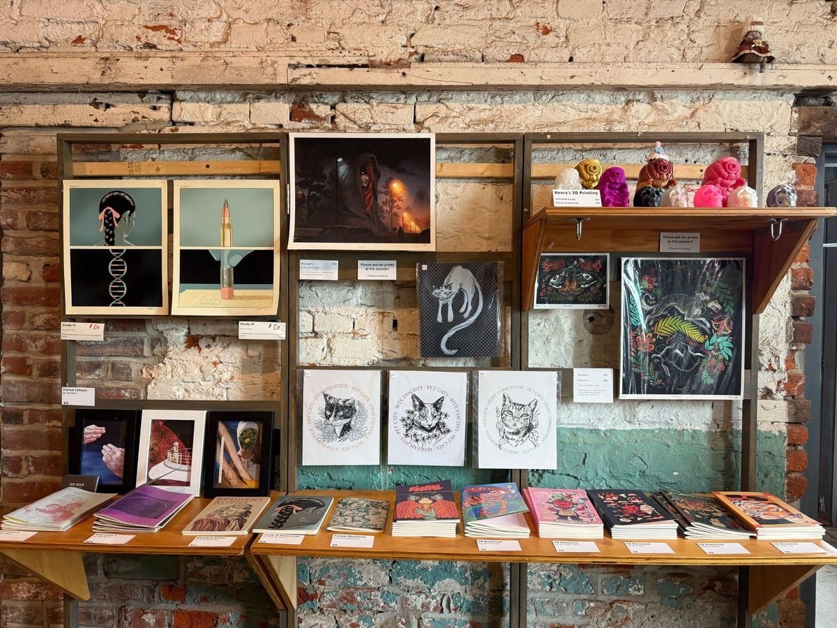 A retail display at Fireball Printing featuring art prints, zines, comic books and ceramic figures against an exposed brick wall.