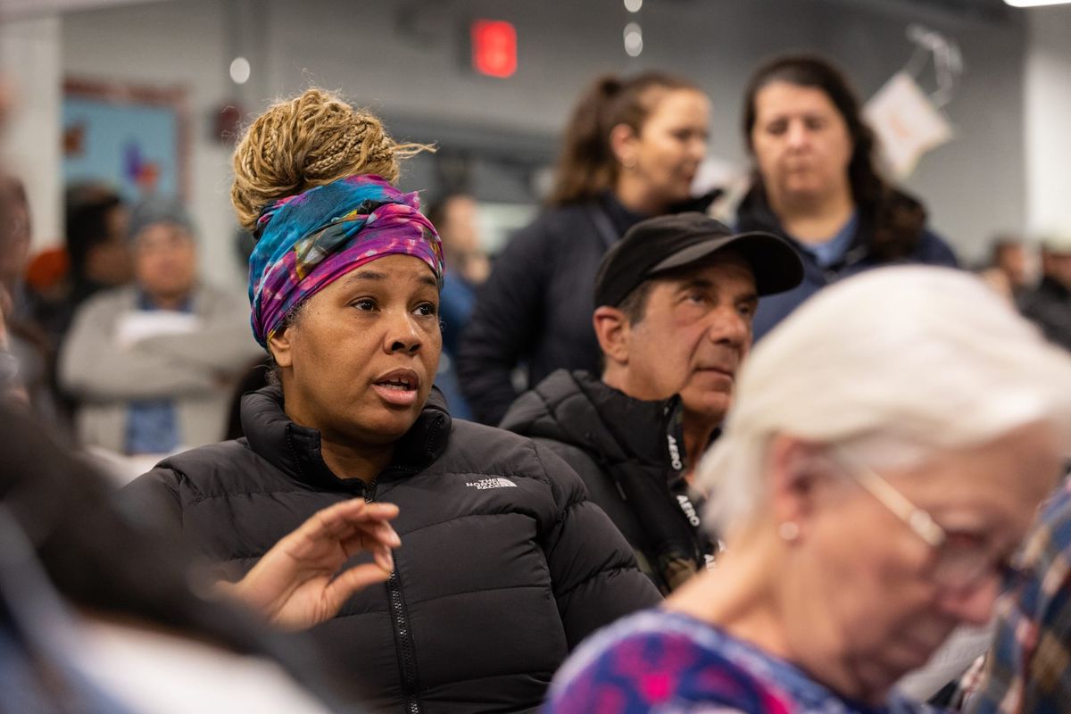 A woman wearing a colorful headwrap speaks while seated among other residents at a Harrowgate Civic Association meeting in Kensington.