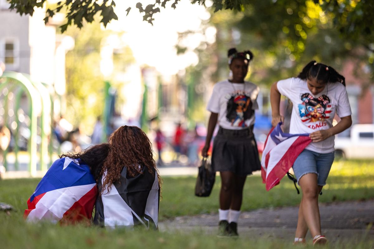 Young people walk through Fairhill Square Park during the Puerto Rican Day Parade in September 2025, while others rest wearing Puerto Rican flags draped around their shoulders.