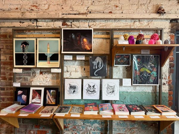 A retail display at Fireball Printing featuring art prints, zines, comic books and ceramic figures against an exposed brick wall.