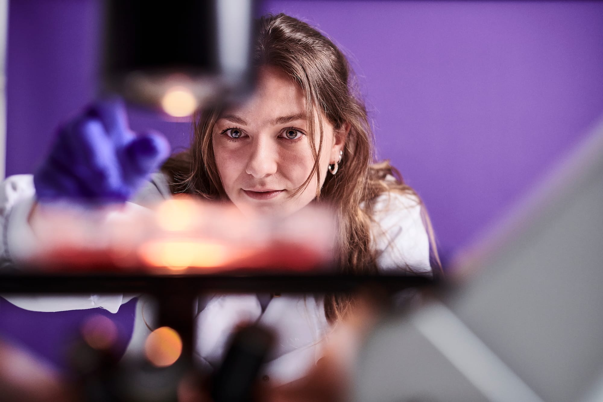 Female scientist from the Scarlet Therpeutics team in a lab coat and gloves adjusting a microscope stage 