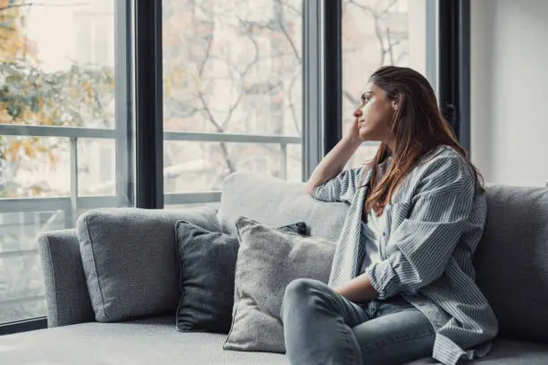 Woman sitting thoughtfully on a couch looking out a window